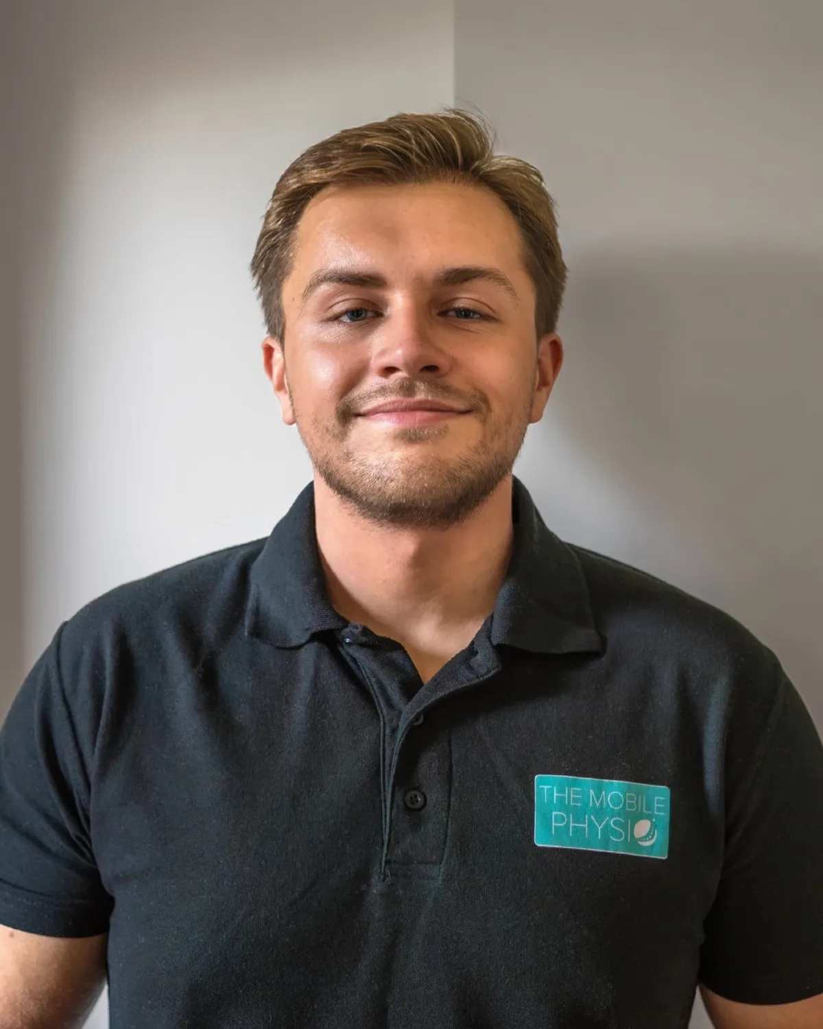 Max Gaffney, founder and physiotherapist at The Mobile Physio, smiling, in a Mobile Physio polo shirt.