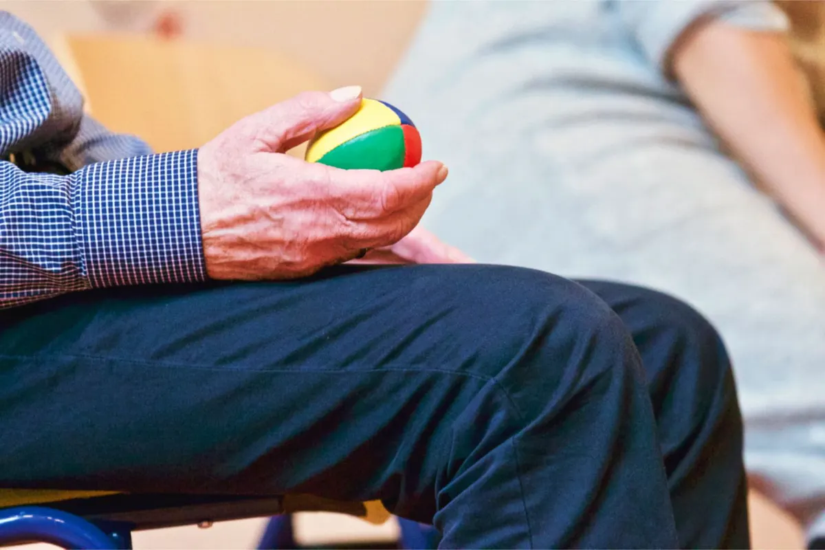 A seated person gripping a small, brightly coloured exercise ball in one hand.